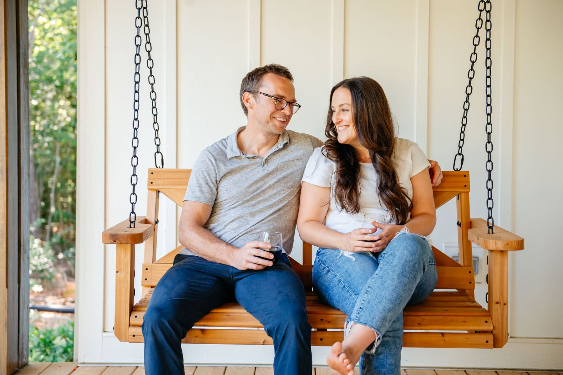 Couple sitting on an outdoor patio swing drinking beer.