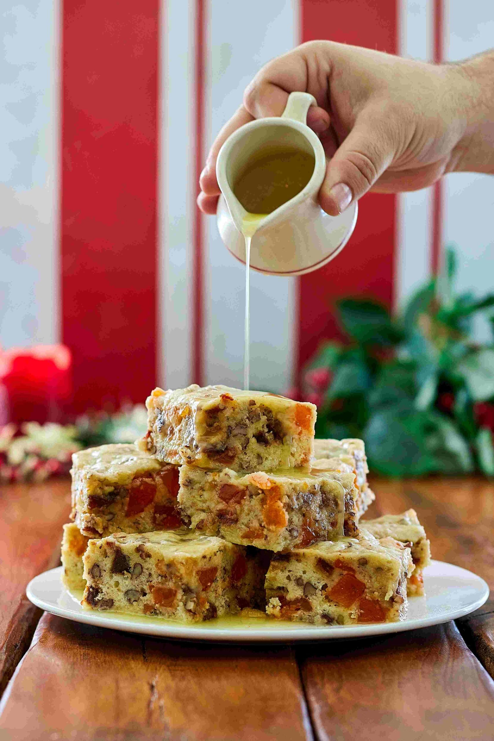 A hand pours glaze from a sauce pitcher over square slices of orange slice cake