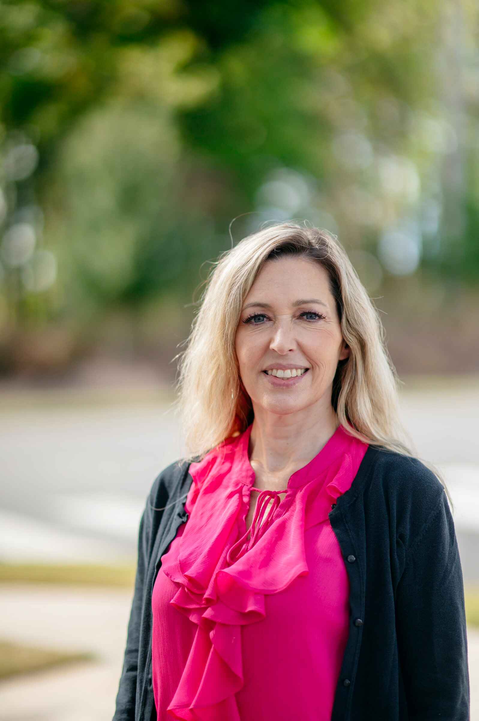 Physician assistant Amy Gonzales of FirstHealth Family Medicine in Pittsboro stands for a portrait in front of a blurred background with green foliage.