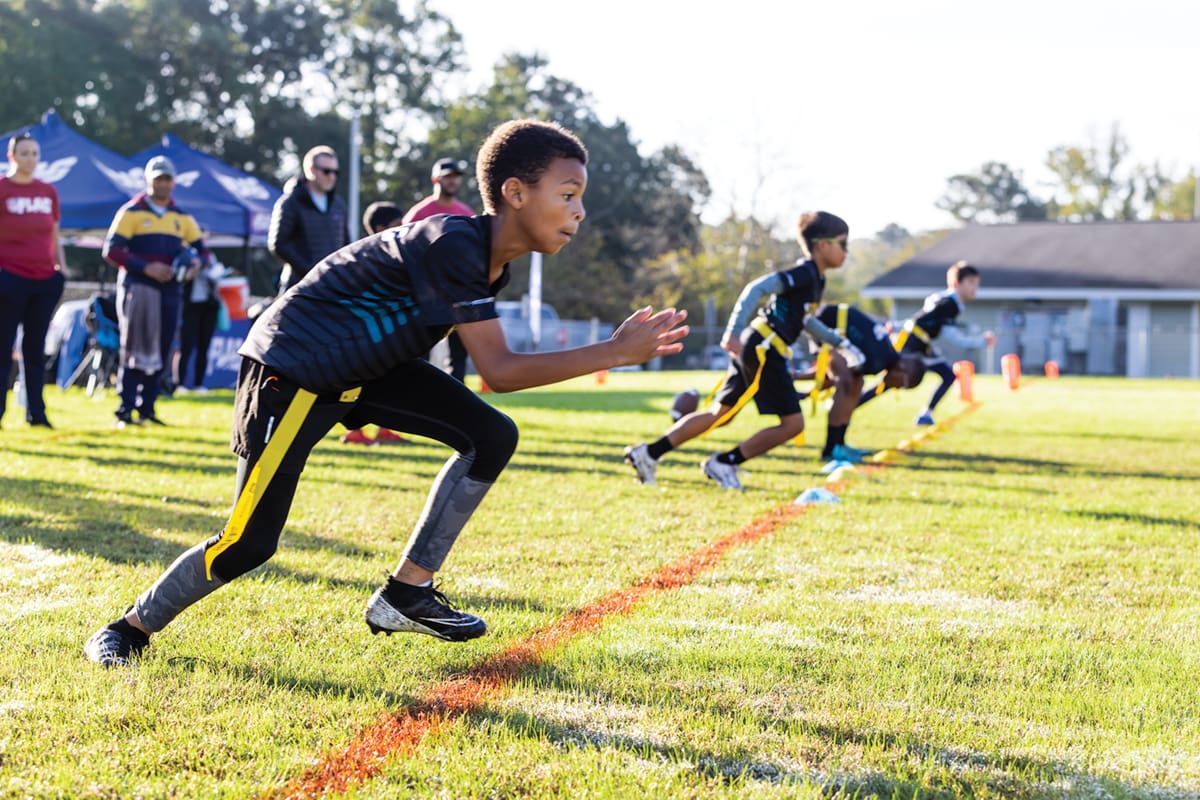 Youth flag football players burst off the line on a field.