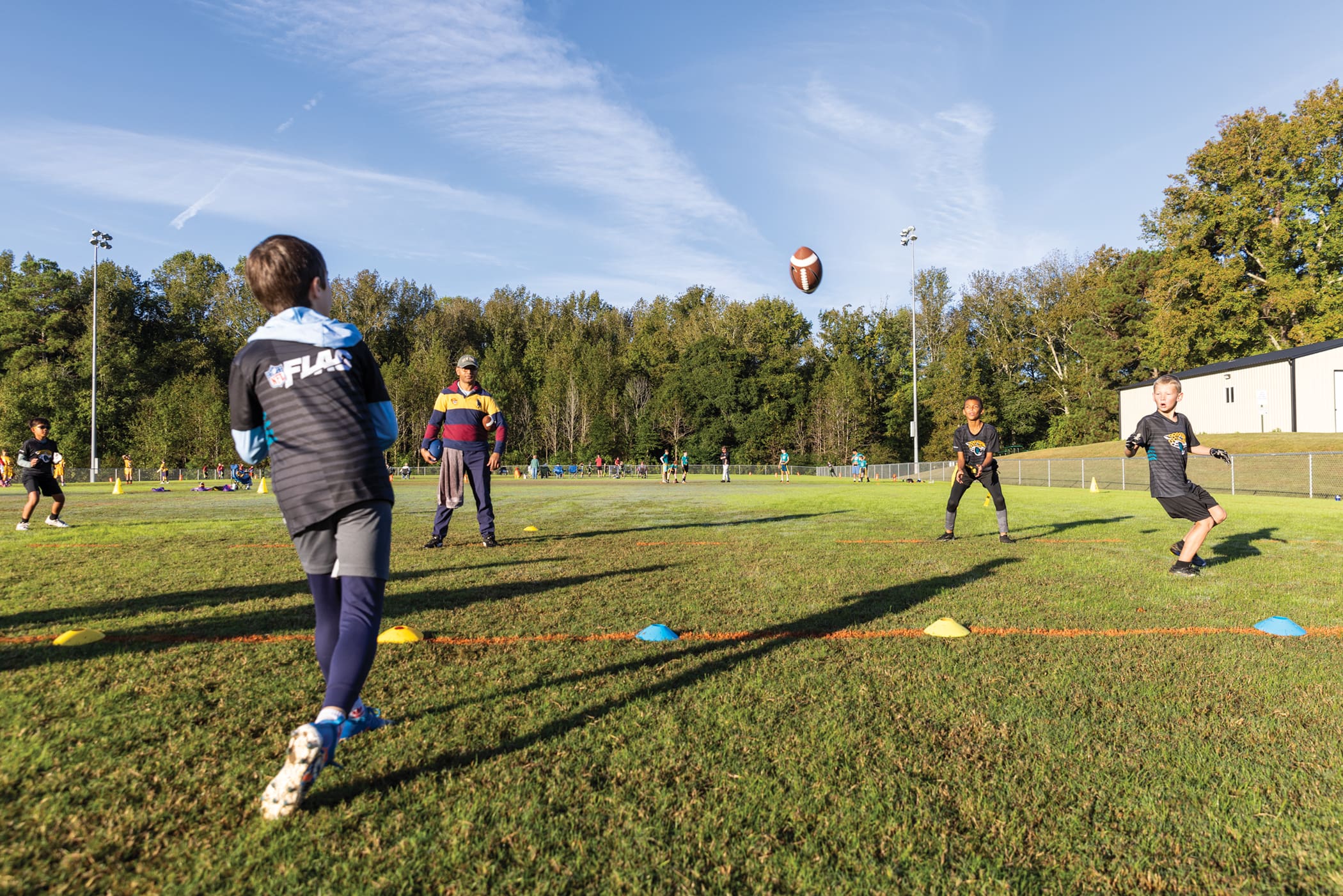 One youth flag football player passes the ball to another across a field.