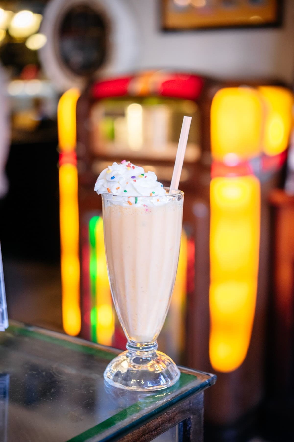 A chocolate milkshake with whipped cream and rainbow sprinkles in a classic milkshake glass