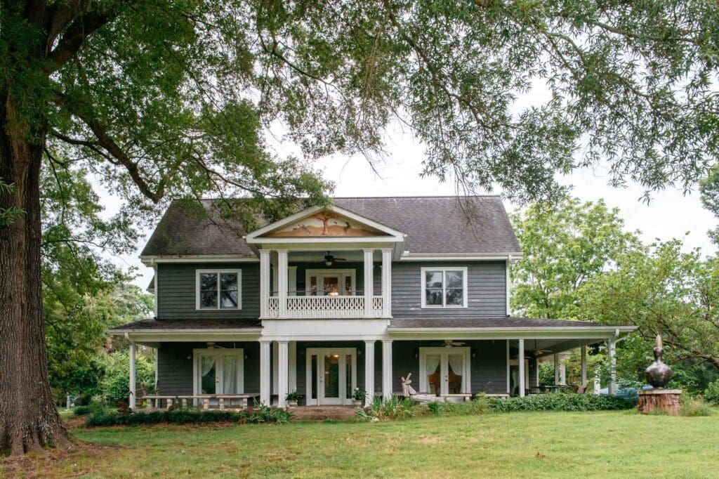The Inn at Celebrity Dairy surrounded by mature trees and a wide front porch in rural North Carolina.