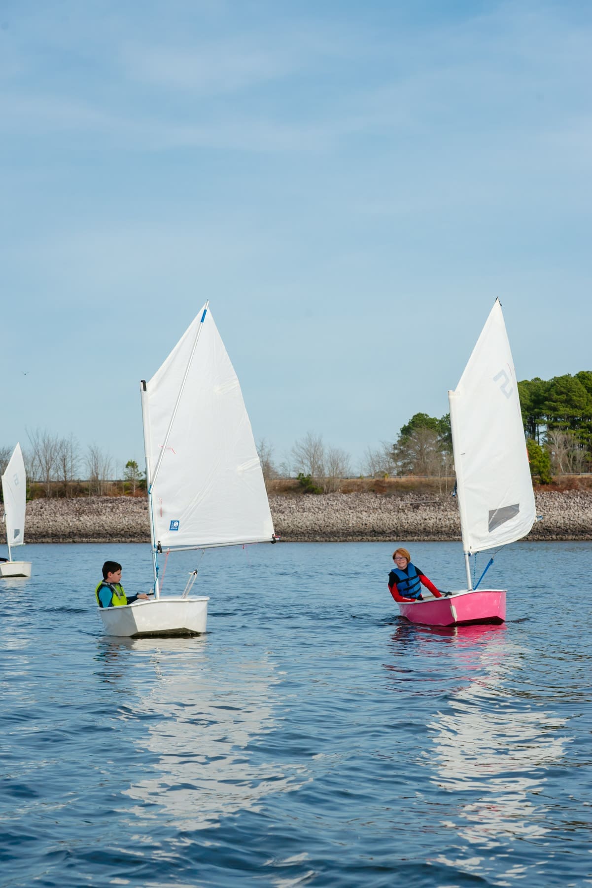 Two sailboats from Carolina Sailing Foundation glide across the glistening Jordan Lake water.