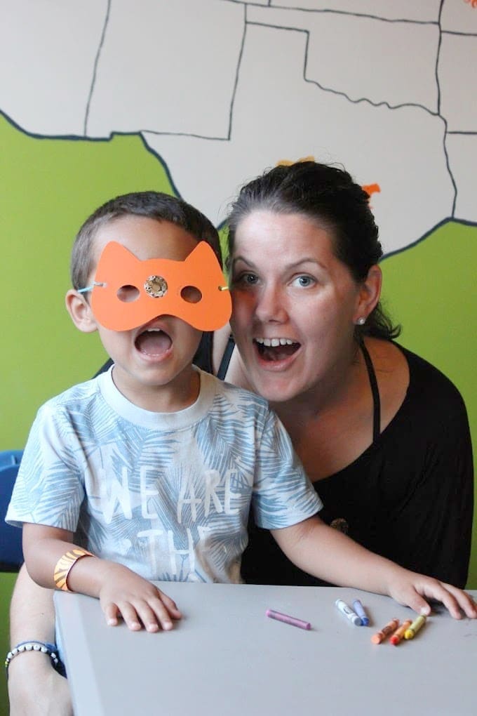 A young boy smiles at the camera with a paper animal mask on his face. A woman smiles next to him at Carolina Tiger Rescue.