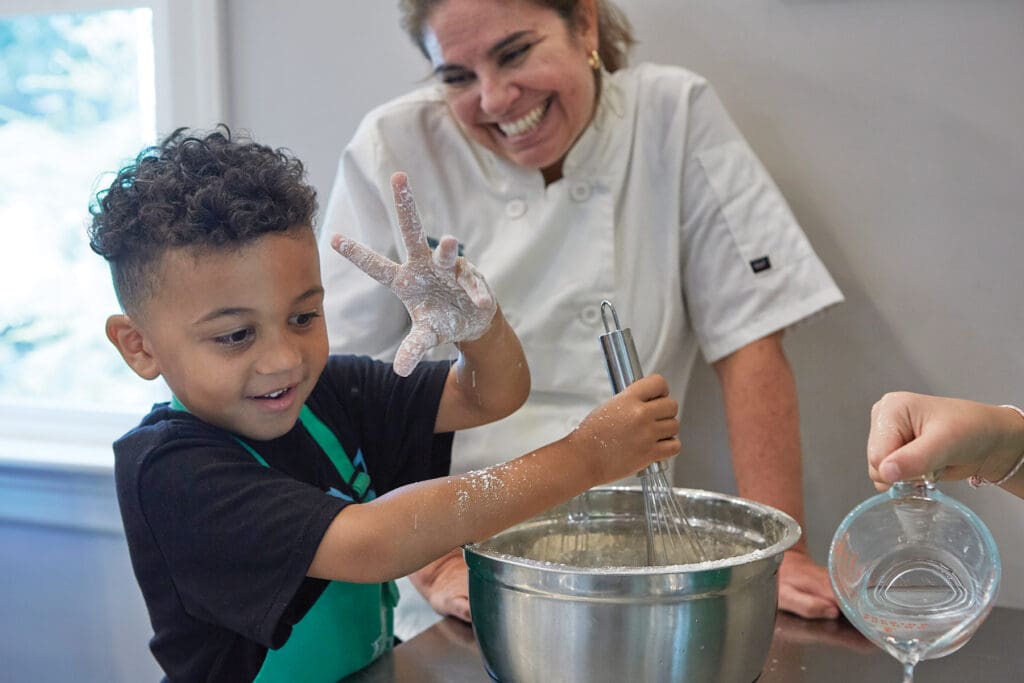 Chef Arlena Strode watching a child mix batter.