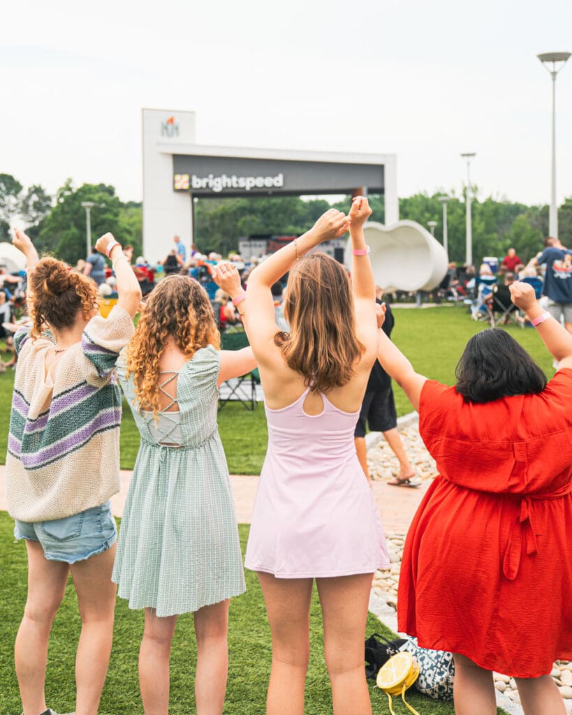 A group of girls dance on a lawn in front of brightspeed arch.